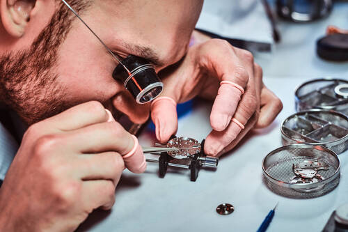 Expirienced clockmaster is fixing old watch for a customer at his repairing workshop.